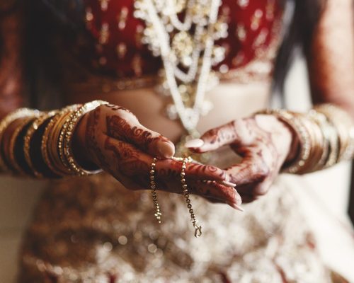 Closeup of Indian bride's hands covered with mehndi and holding a golden necklace