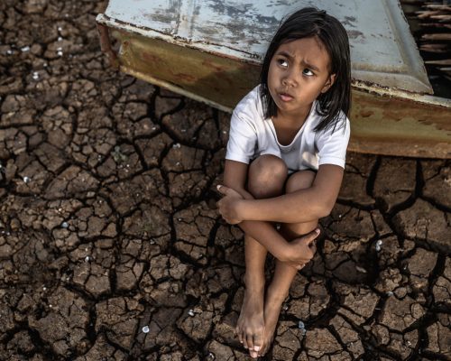 hugging their knees and looking at the sky on dry soil and there are fishing boats, global warming.